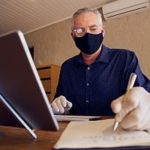 Small business owner in mask on computer