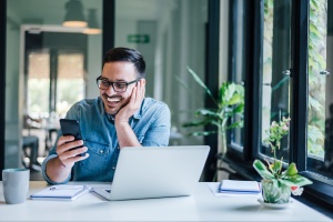 Smiling businessman using phone in home or office. Small business entrepreneur looking at his mobile phone and smiling reading or texting good news.